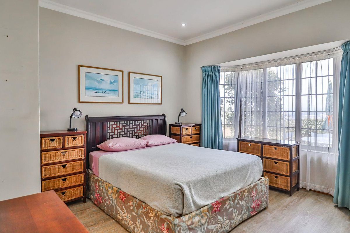 A well-lit bedroom featuring a large bay window with natural light, neutral wall tones, and wood-look flooring.