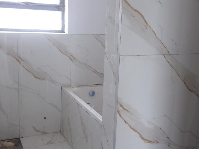 A bathroom under renovation featuring marble-look wall and floor tiles with a built-in bathtub, currently awaiting final plumbing fixtures and floor finishing.