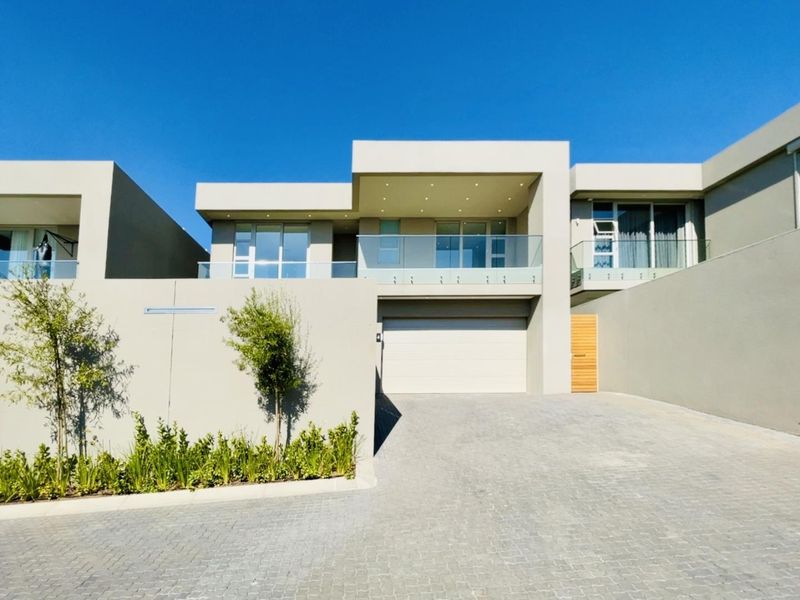 Modern double-story cluster home featuring a paved driveway, integrated garage, and a sleek balcony with glass balustrades.