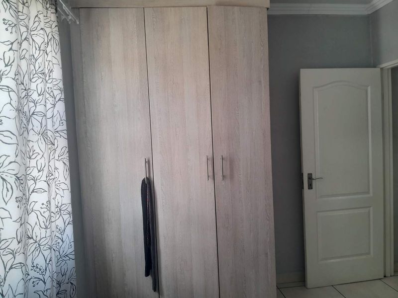 A bedroom featuring a light wood-finish built-in wardrobe, a white panel door, and neutral tiled flooring.