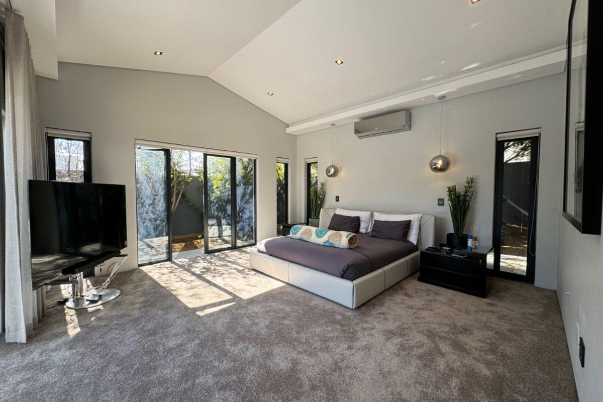 Spacious bedroom featuring high vaulted ceilings, recessed lighting, wall-mounted air conditioning, and large sliding glass doors providing direct access to the garden.