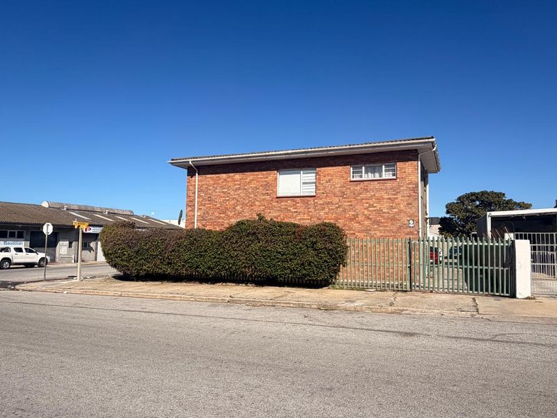 Exterior view of a brick apartment building featuring metal security fencing and a concrete driveway, situated on a street corner.