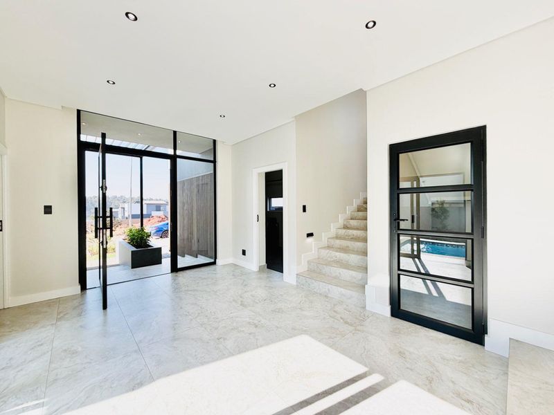 Modern, spacious entrance hall featuring large-format stone floor tiles, recessed lighting, and a contemporary staircase with glass-panelled doors leading to the exterior.