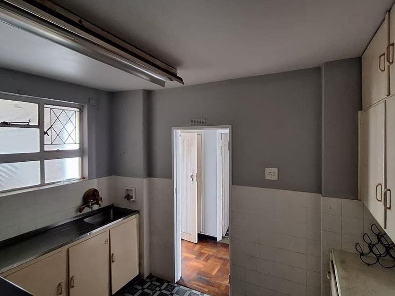 A dated kitchen featuring original built-in cabinetry, a stainless steel sink, and tiled splashbacks, offering significant potential for a modern renovation.