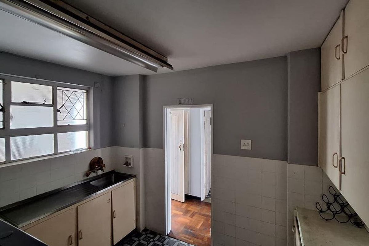 A dated kitchen featuring original built-in cabinetry, a stainless steel sink, and tiled splashbacks, offering significant potential for a modern renovation.