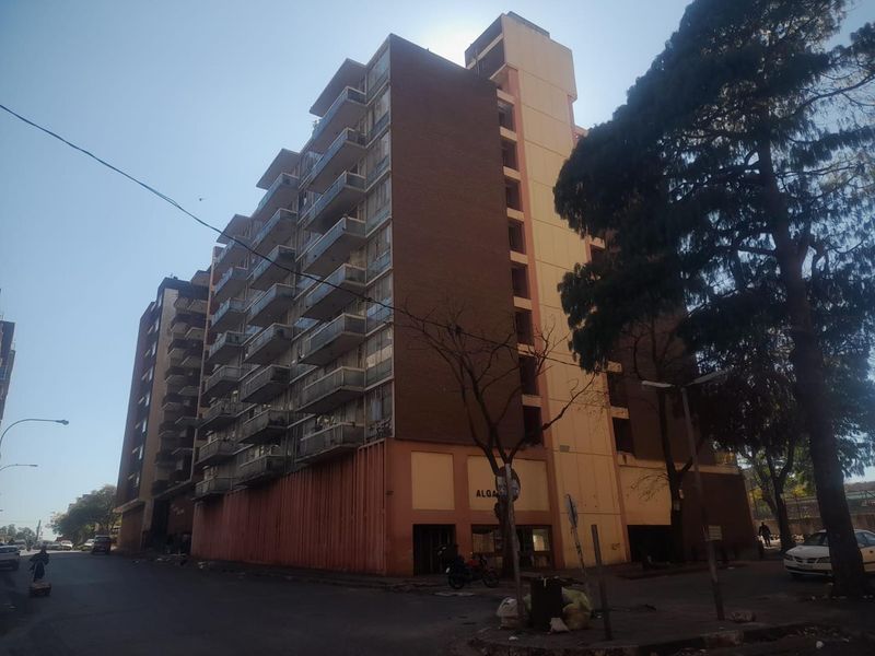 A multi-story apartment building exterior featuring stacked balconies with glass balustrades, viewed from the street level.