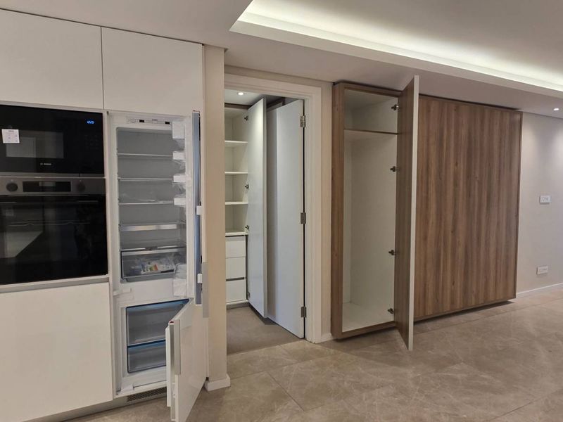 Modern open-plan living area featuring a sleek kitchen with integrated appliances, stone countertops, recessed lighting, and ample built-in storage cabinetry.