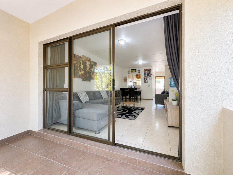 A covered balcony with tiled flooring featuring a large sliding glass door providing access to the open-plan living and dining area.
