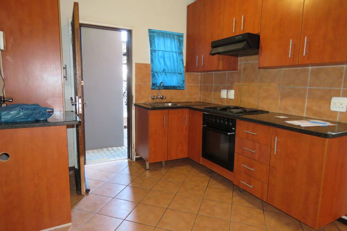 A functional kitchen featuring wooden cabinetry, dark countertops, a built-in oven with hob, and an extractor fan, with direct access to an outdoor area.