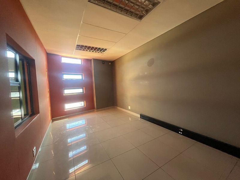 An empty office space featuring tiled flooring, recessed ceiling lighting, and multiple small windows providing natural light.