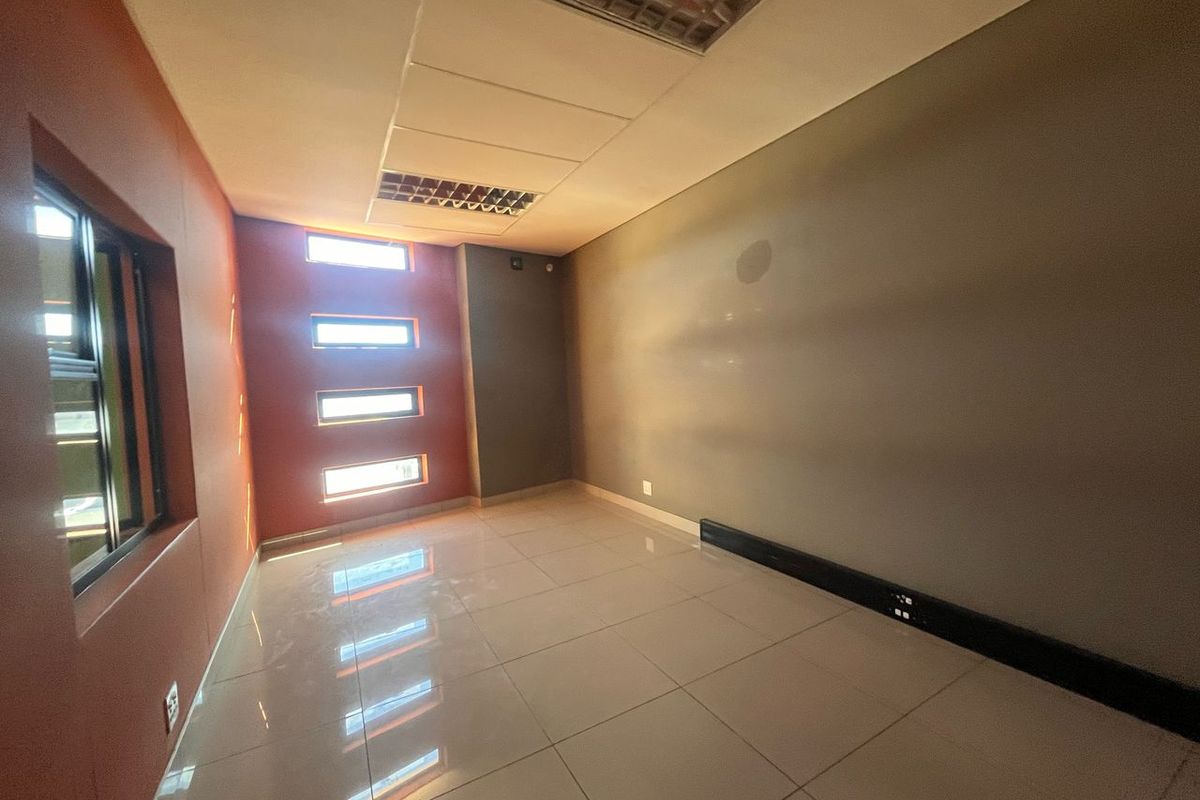 An empty office space featuring tiled flooring, recessed ceiling lighting, and multiple small windows providing natural light.