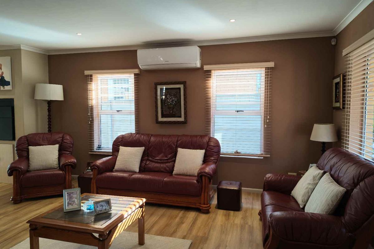 A comfortable living room featuring wood-look flooring, recessed downlighting, venetian blinds, and a wall-mounted air conditioning unit.