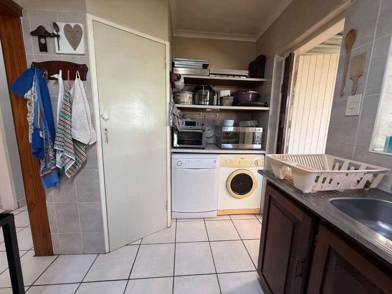 A functional scullery area featuring tiled flooring, built-in shelving for storage, and a stainless steel sink with tiled splashback.