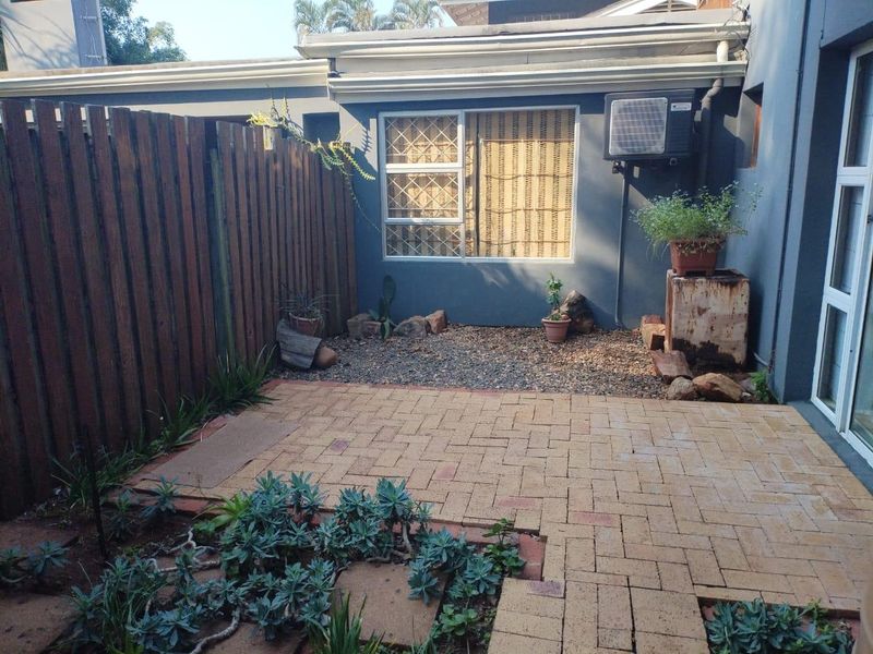 A private paved patio area featuring a timber fence, security-barred window, and wall-mounted air conditioning unit, offering a low-maintenance outdoor space.