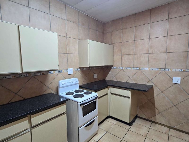 A functional kitchen featuring built-in cabinetry, granite countertops, and a freestanding stove, finished with full-height ceramic wall tiling.
