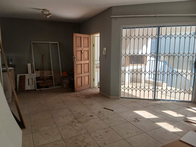 An empty living area featuring tiled flooring, a security gate leading to a patio with a built-in braai, and an intercom system.