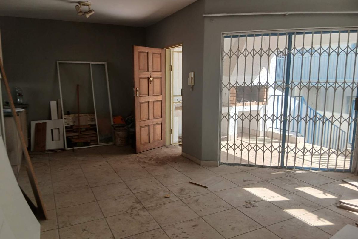 An empty living area featuring tiled flooring, a security gate leading to a patio with a built-in braai, and an intercom system.