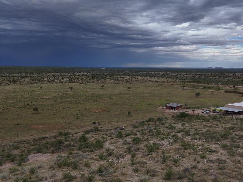 An aerial view of a large farm property featuring expansive open land, fenced paddocks, and existing farm buildings under a dramatic cloudy sky.
