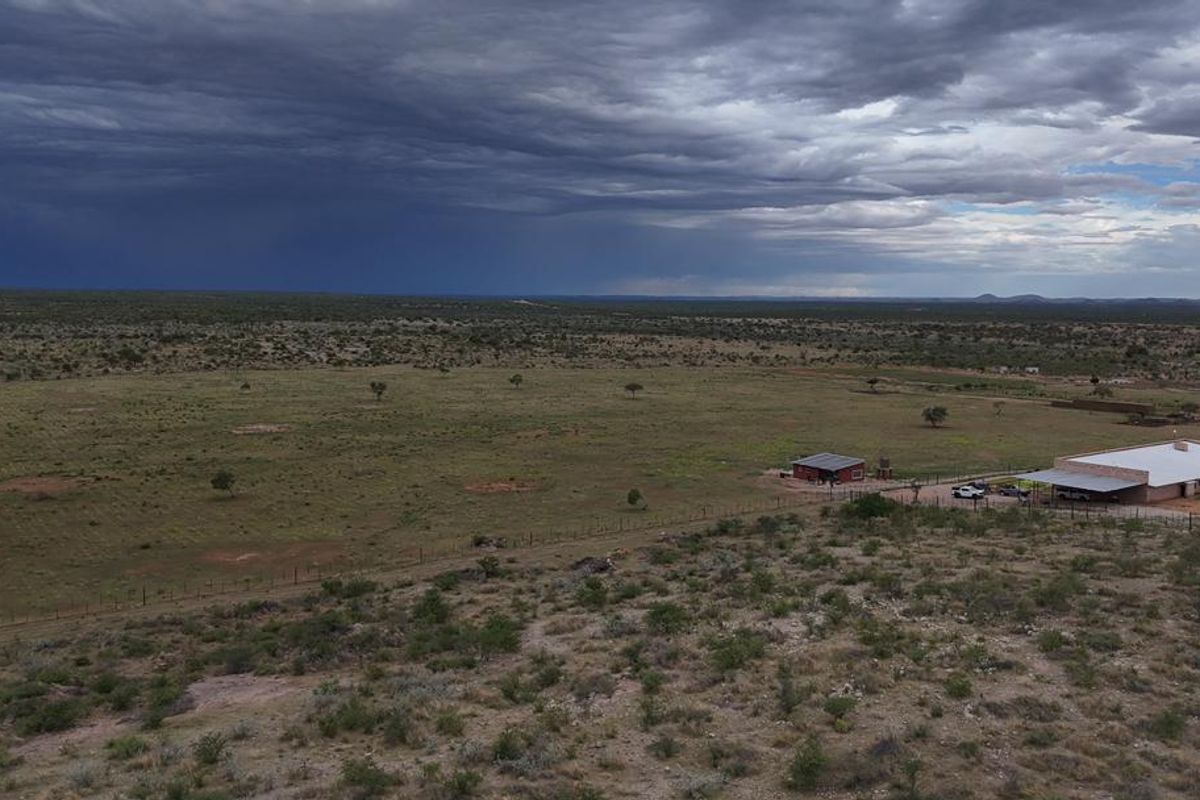 An aerial view of a large farm property featuring expansive open land, fenced paddocks, and existing farm buildings under a dramatic cloudy sky.