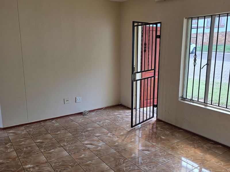 An empty living room featuring ceramic tile flooring, a security gate, and burglar bars on the window.