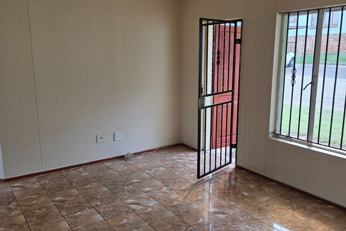 An empty living room featuring ceramic tile flooring, a security gate, and burglar bars on the window.