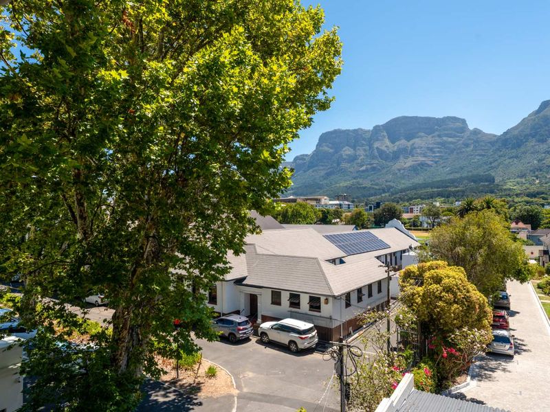 Elevated view overlooking the property grounds, featuring a tiled roof with solar panels, surrounding trees, and a scenic mountain backdrop.