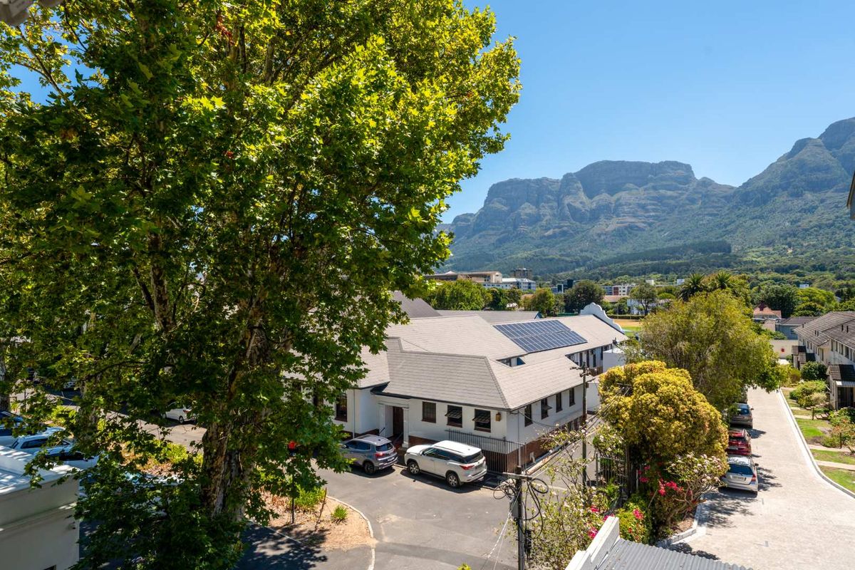 Elevated view overlooking the property grounds, featuring a tiled roof with solar panels, surrounding trees, and a scenic mountain backdrop.