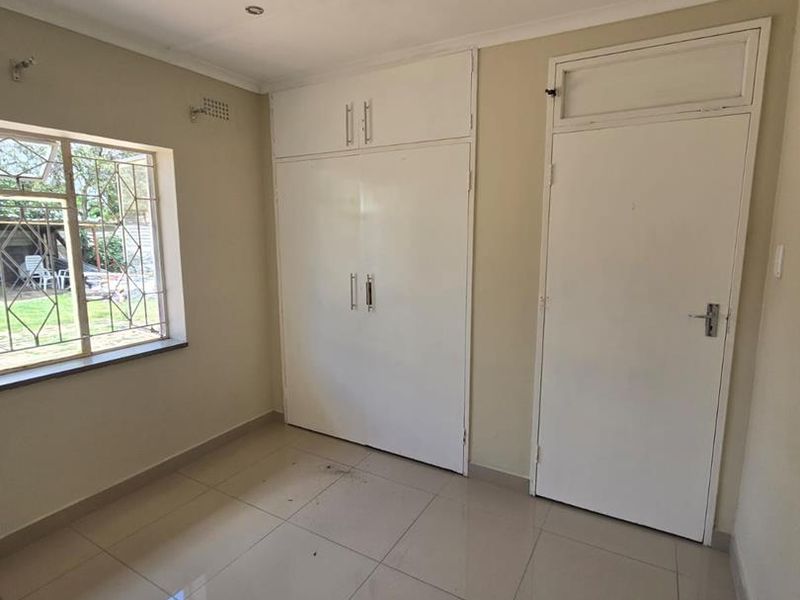 A vacant bedroom featuring tiled flooring, built-in cupboards, and security bars on the window, offering a clean canvas for potential updates.