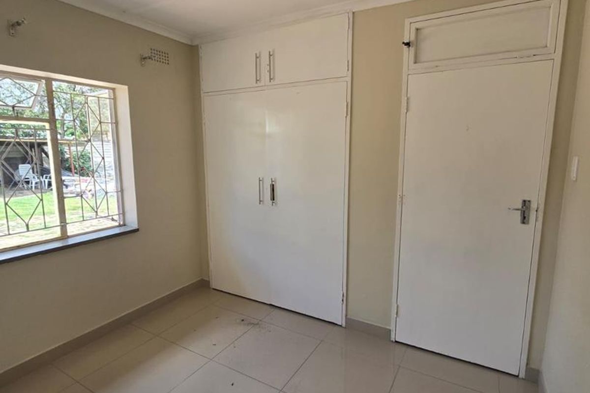 A vacant bedroom featuring tiled flooring, built-in cupboards, and security bars on the window, offering a clean canvas for potential updates.