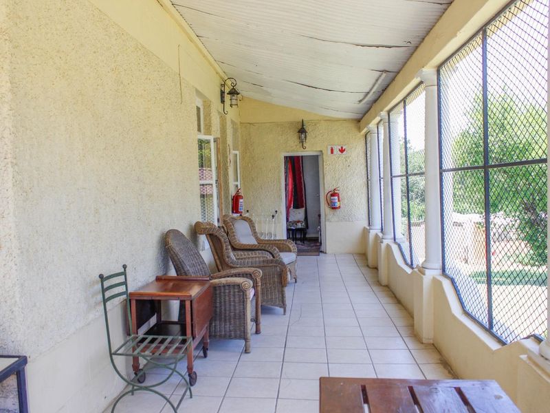 A covered patio area featuring tiled flooring, security mesh screening, and wall-mounted lighting, providing a functional outdoor space for the guest house.