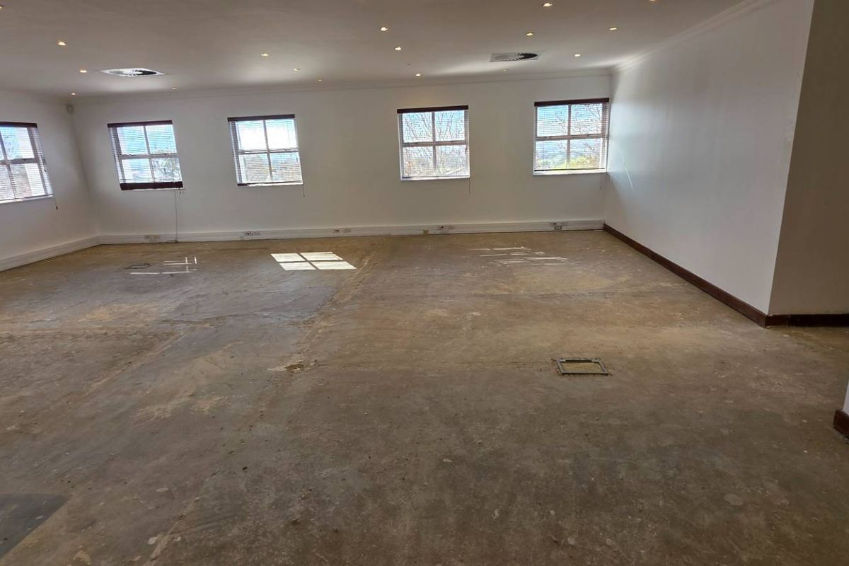 A spacious, empty office area featuring multiple windows, recessed lighting, and floor power outlets, currently requiring new flooring installation.