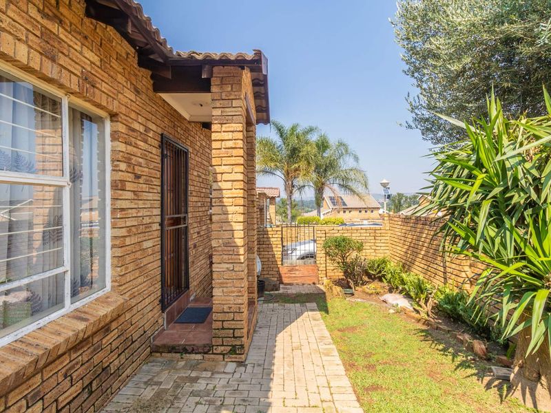 A rear exterior view of a face brick townhouse featuring a paved walkway, small garden area, and secure boundary walling.