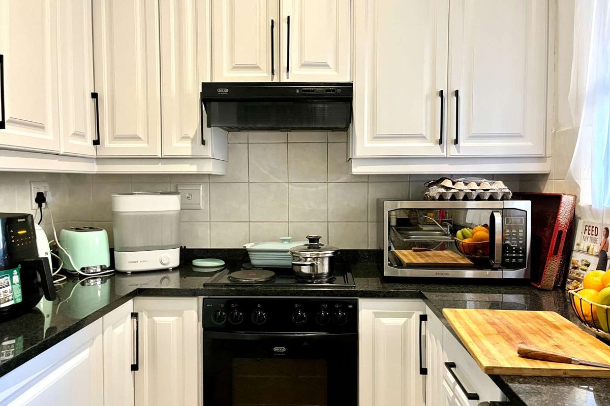 A functional kitchen featuring white cabinetry, dark granite countertops, a built-in oven, electric hob, and a tiled backsplash.