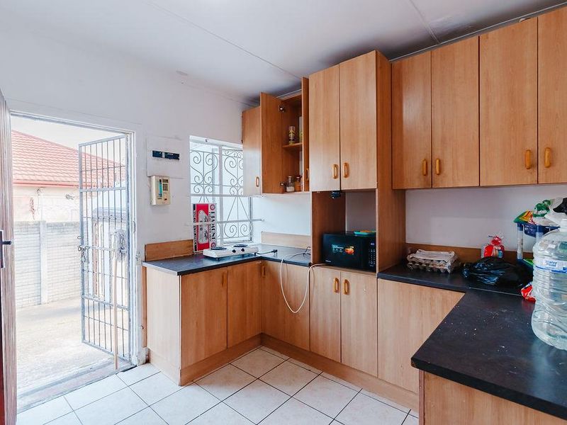 A functional kitchen featuring laminate cabinetry, dark countertops, tiled flooring, and direct access to the exterior through a security gate.