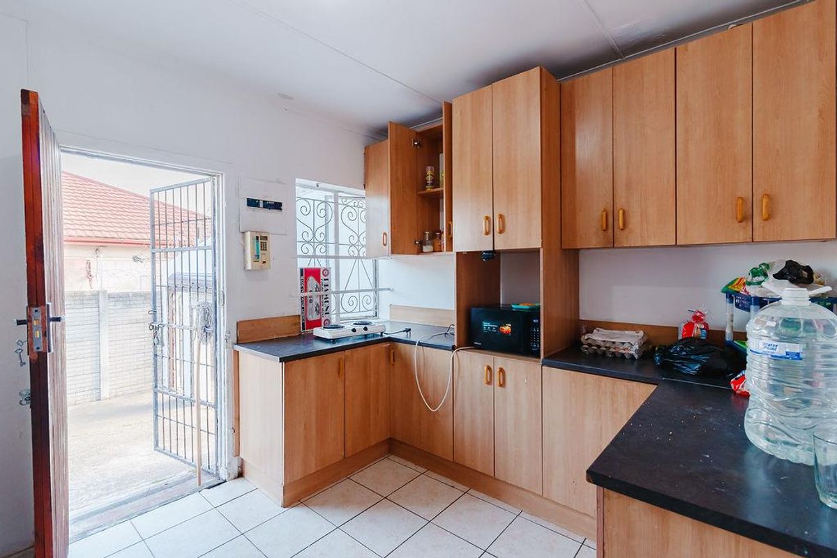 A functional kitchen featuring laminate cabinetry, dark countertops, tiled flooring, and direct access to the exterior through a security gate.