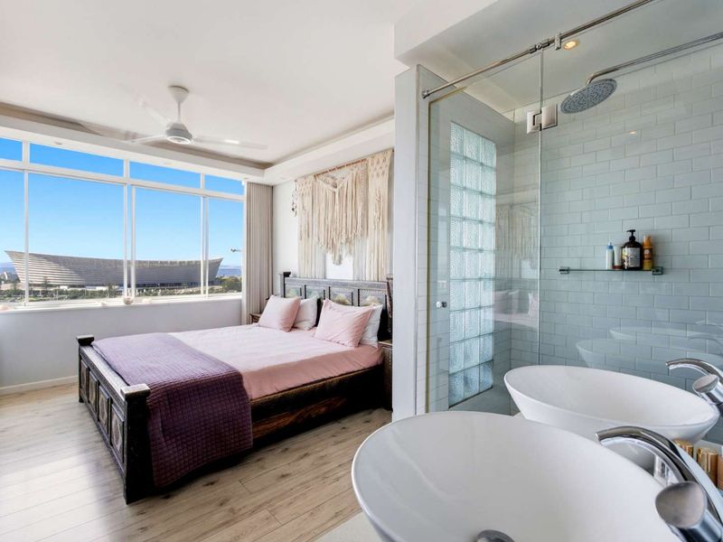 Modern bedroom featuring an open-plan en-suite bathroom with a glass-enclosed shower, dual vanity basins, and expansive windows offering scenic views.