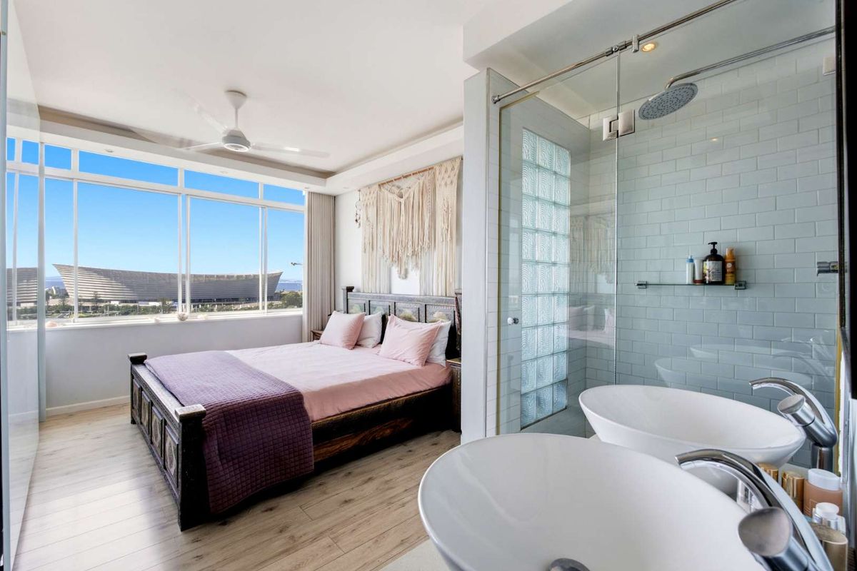 Modern bedroom featuring an open-plan en-suite bathroom with a glass-enclosed shower, dual vanity basins, and expansive windows offering scenic views.