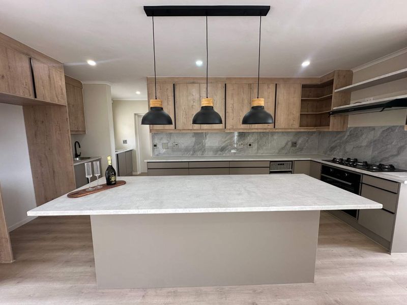 Modern kitchen featuring a central island, stone countertops, wood-finish cabinetry, integrated appliances, and stylish pendant lighting in an open-plan layout.