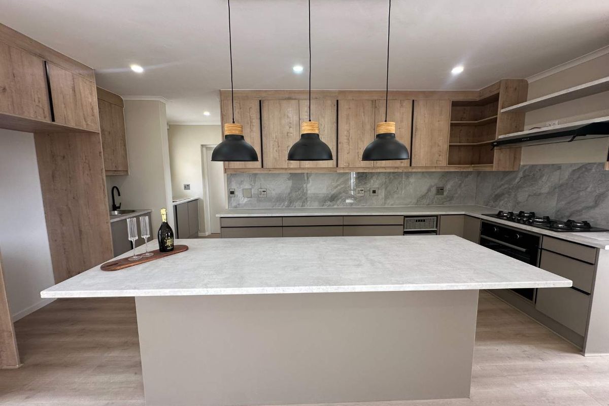 Modern kitchen featuring a central island, stone countertops, wood-finish cabinetry, integrated appliances, and stylish pendant lighting in an open-plan layout.