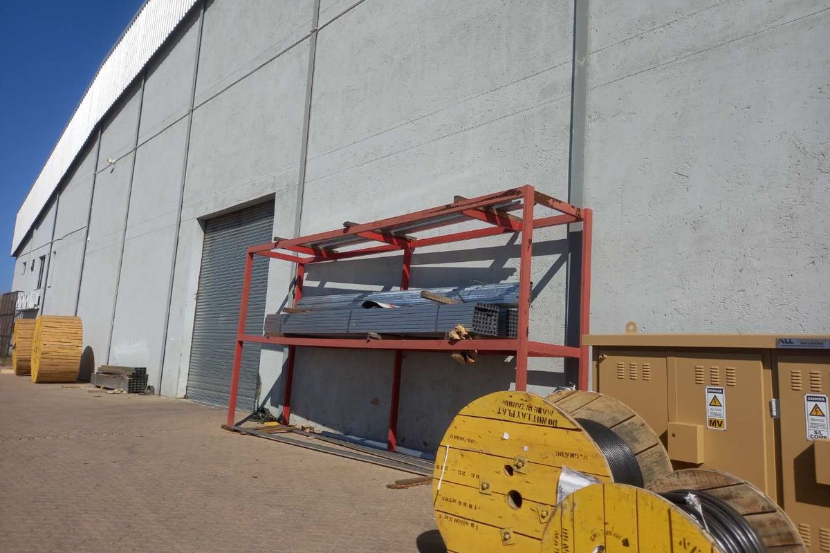 Industrial exterior view showing a large warehouse facade with a roller shutter door, concrete walling, and paved yard area.
