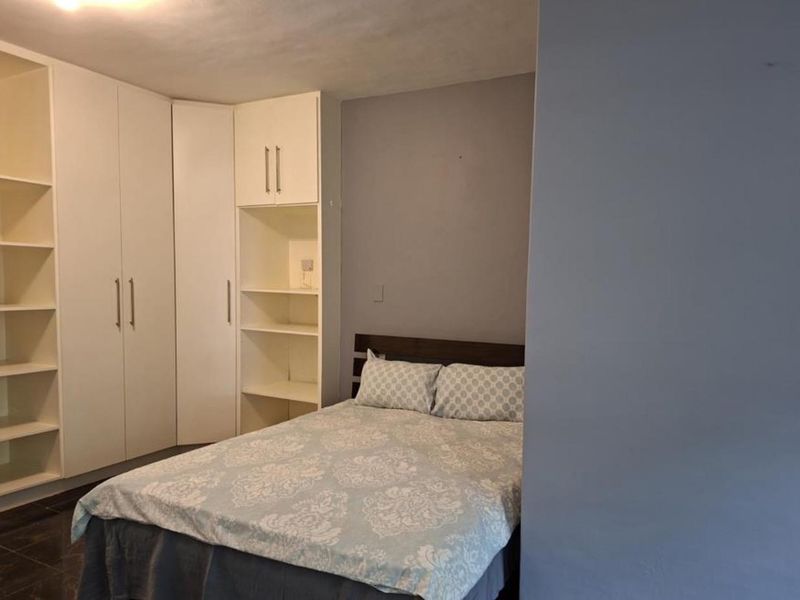 A bedroom featuring white built-in cupboards and integrated shelving units, providing ample storage space.