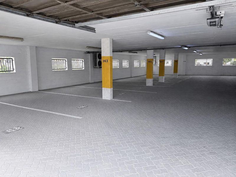 A clean, well-maintained covered parking garage featuring paved flooring, structural support columns, and secure window grilles.
