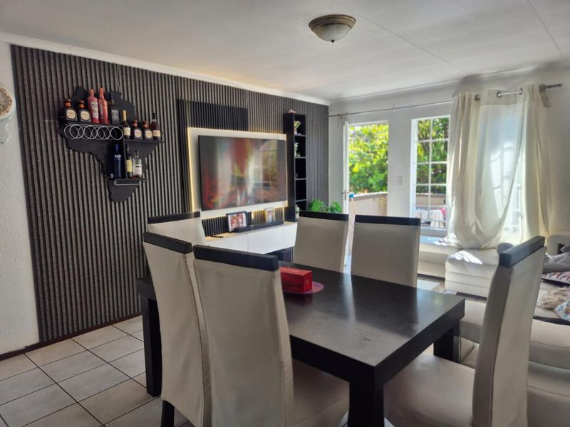 Open plan living and dining area featuring decorative slatted wall paneling, tiled flooring, and direct access to an outdoor balcony through french doors.