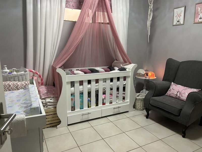 A nursery bedroom featuring tiled flooring and neutral wall finishes, currently set up with a crib and seating area.