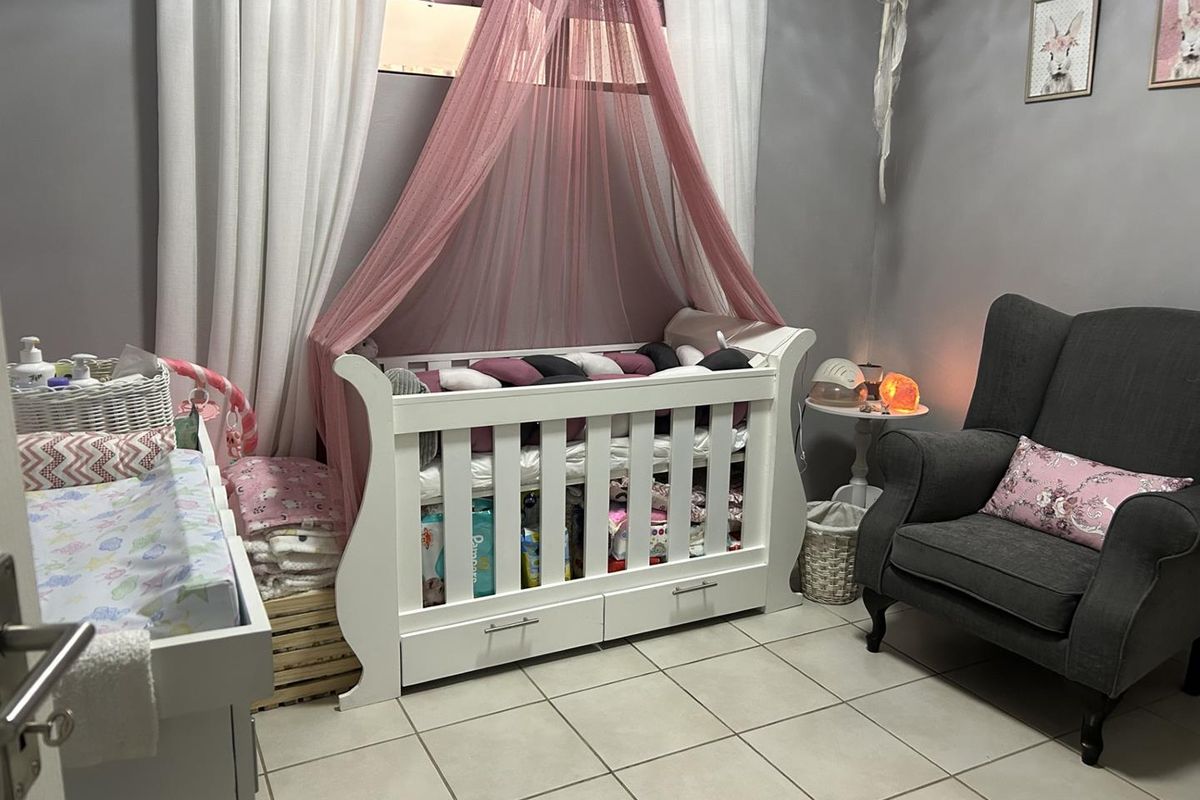 A nursery bedroom featuring tiled flooring and neutral wall finishes, currently set up with a crib and seating area.