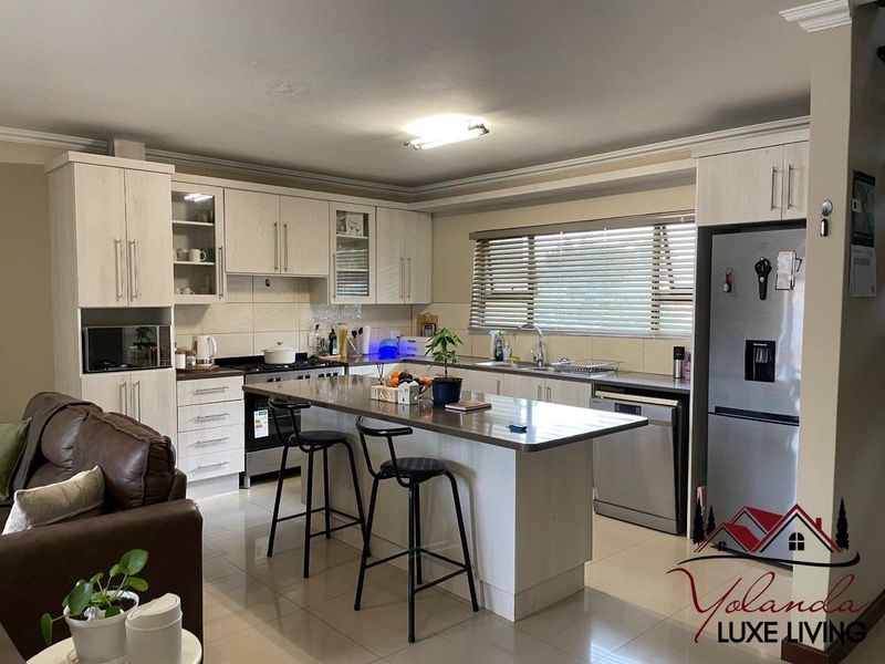 Open plan kitchen featuring light wood cabinetry, a central island with breakfast bar seating, tiled flooring, and integrated appliances.