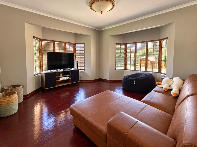 Spacious living room featuring dual bay windows with wooden blinds, polished hardwood flooring, and neutral wall finishes.