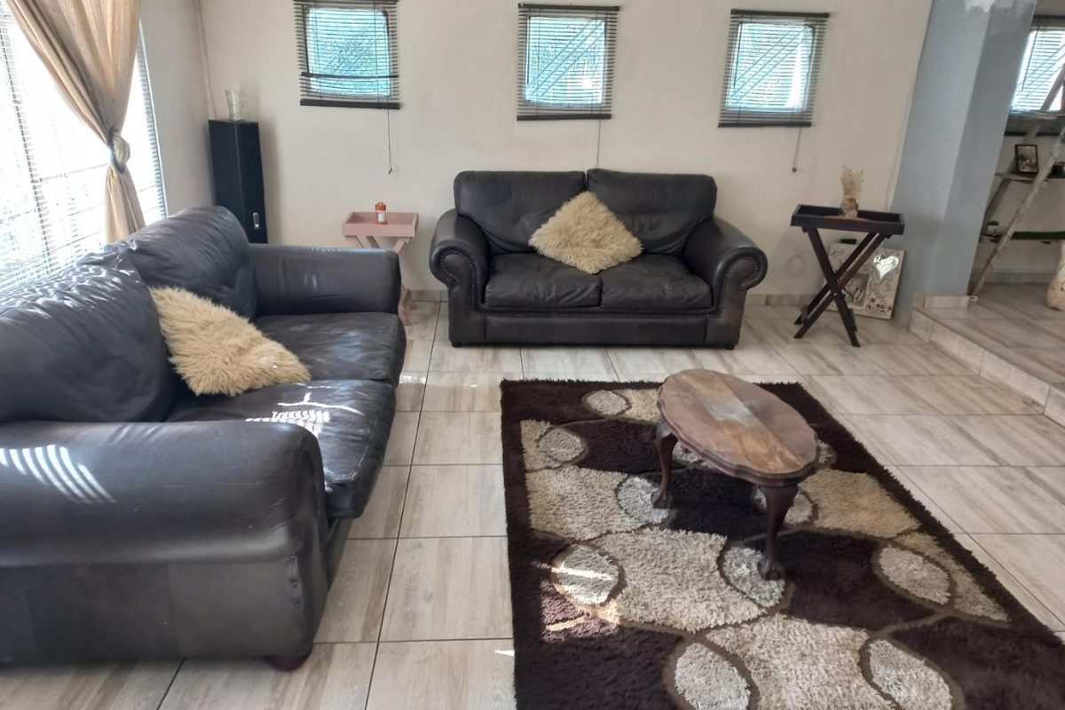A living room featuring tiled flooring and three small windows with venetian blinds, requiring minor cosmetic updates to the wall finishes.
