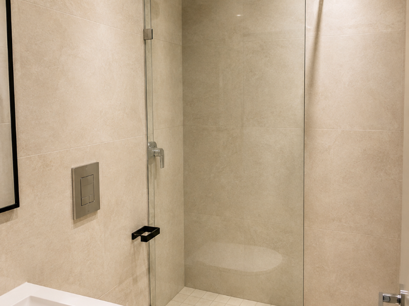 Modern bathroom featuring a walk-in shower with glass screen, wall-mounted toilet, and sleek vanity basin with neutral floor-to-ceiling tiling.