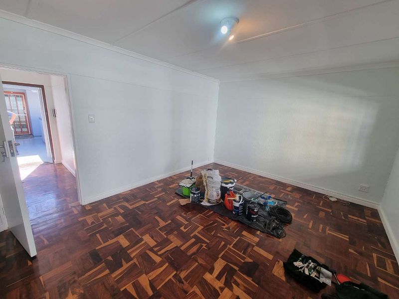 A vacant bedroom featuring classic parquet flooring and neutral walls, currently undergoing minor maintenance or painting.
